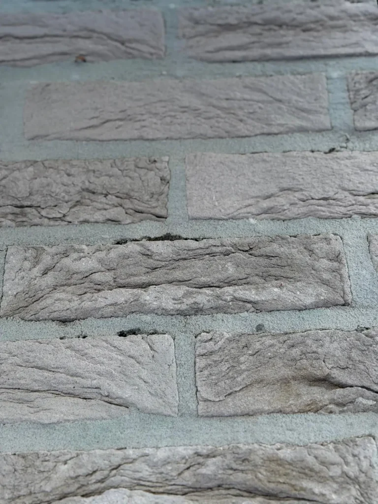Close-up van een muur van grijze bakstenen, met rechthoekige stenen met een ruw, gestructureerd oppervlak en mortel die de openingen ertussen opvult.